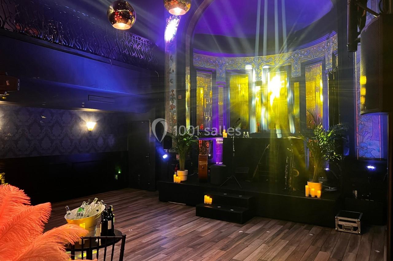 Salle de spectacle avec scène éclairée, décor art déco, parquet au sol, bougies et plantes en décoration.
