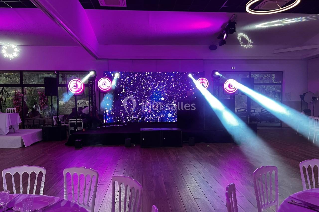 Salle de réception avec éclairage violet, scène équipée d'écrans lumineux et projecteurs diffusant des faisceaux lumineux.