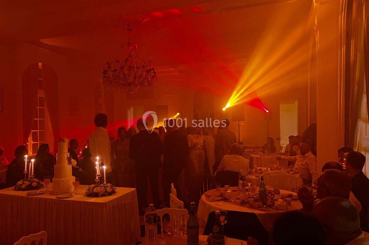 Salle de réception éclairée par des lumières colorées, avec des invités rassemblés près d'une piste de danse.