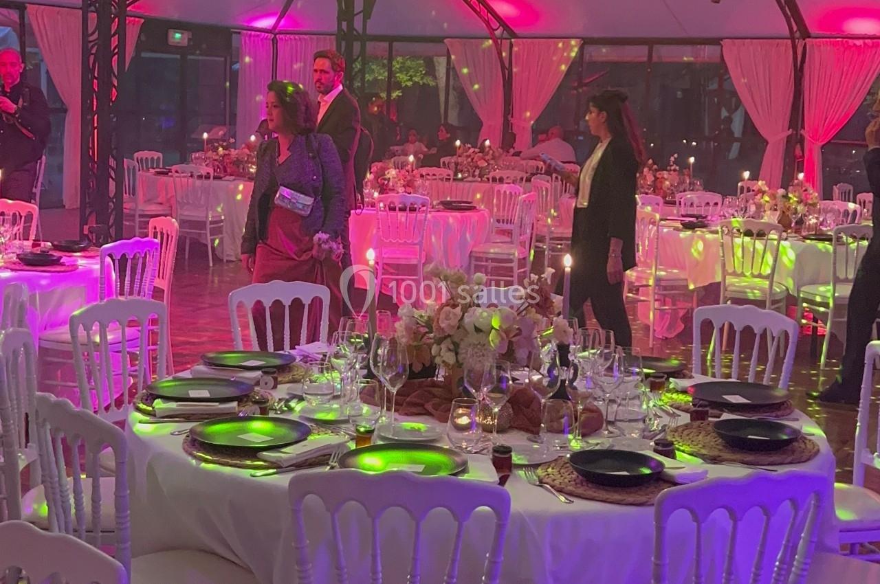 Salle de réception décorée avec des tables dressées, éclairage coloré et invités en tenue de soirée.