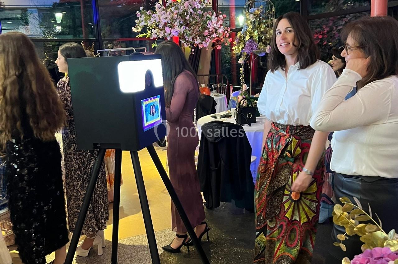 Des personnes posent devant une borne photo lumineuse lors d'un événement festif avec une décoration florale.