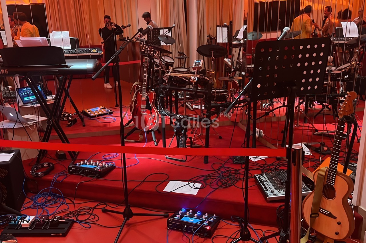 Salle de répétition avec instruments de musique variés, dont claviers, guitares, batterie et matériel audio.