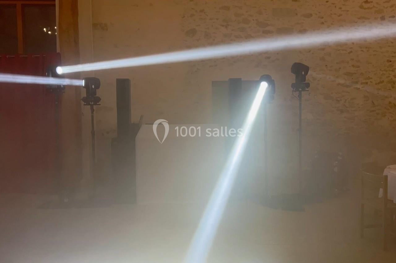 Deux faisceaux lumineux blancs traversent une salle avec des murs en pierre, éclairant un espace légèrement enfumé.