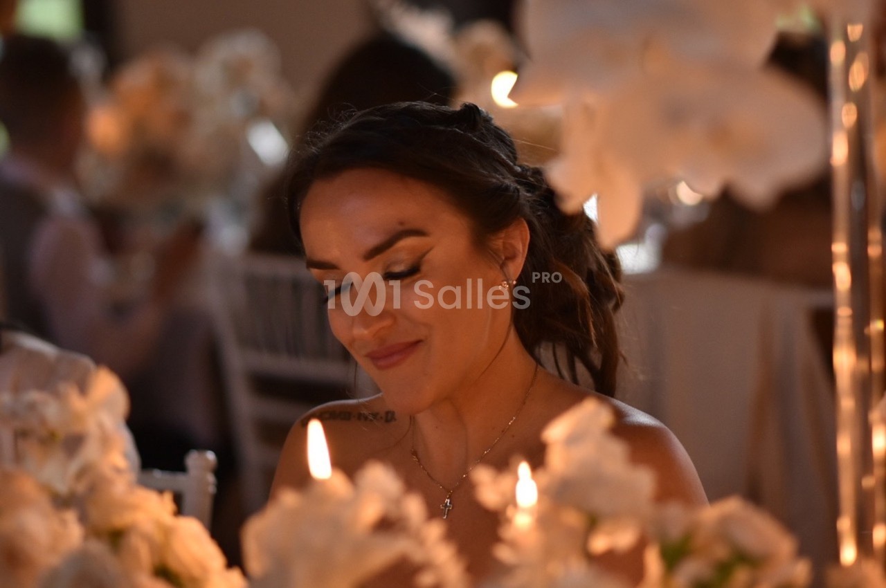 Femme souriante assise à une table décorée de fleurs blanches et éclairée par des bougies.