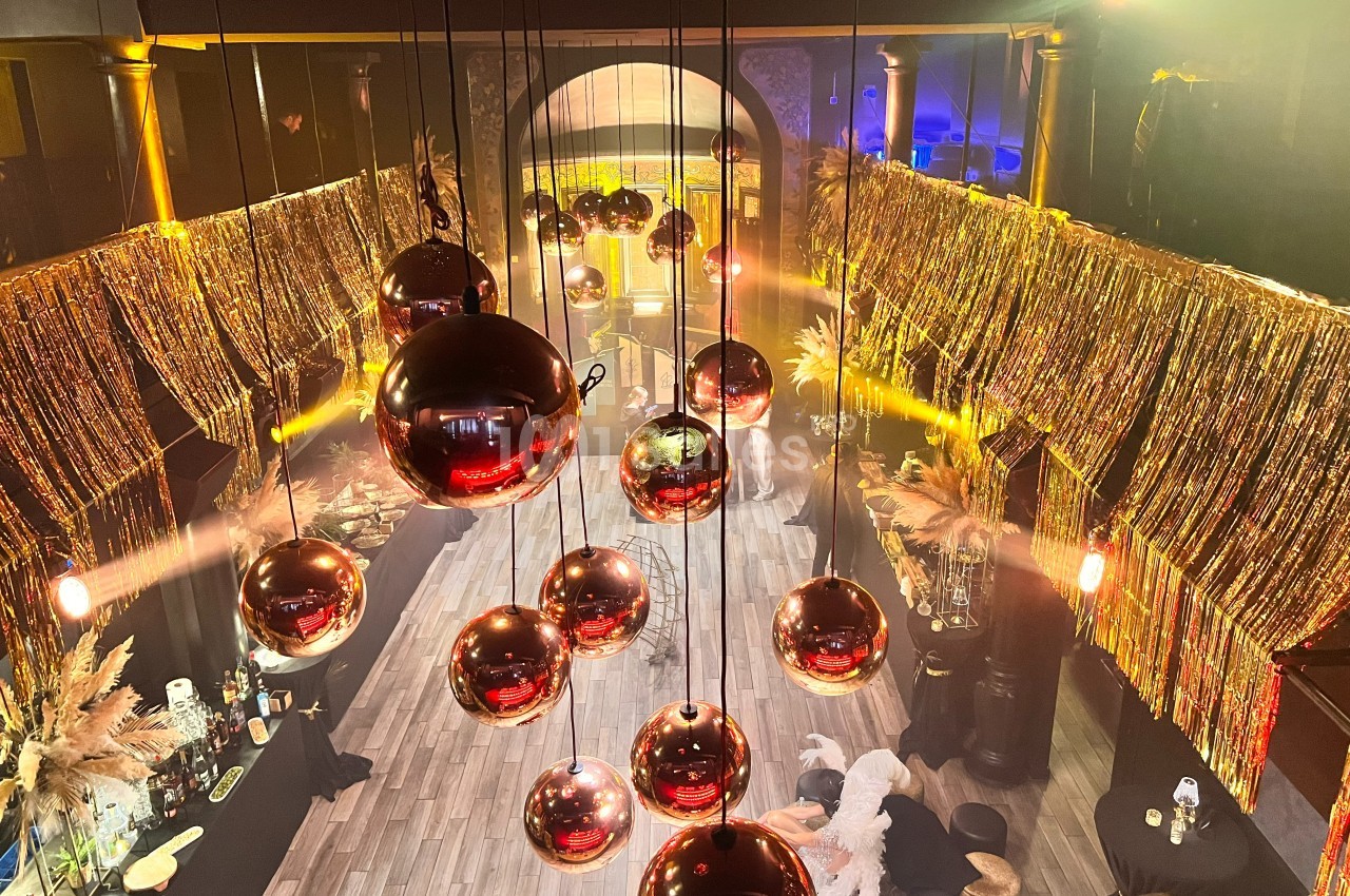 Salle décorée avec des guirlandes dorées et des boules suspendues réfléchissantes, éclairée par des lumières chaudes.