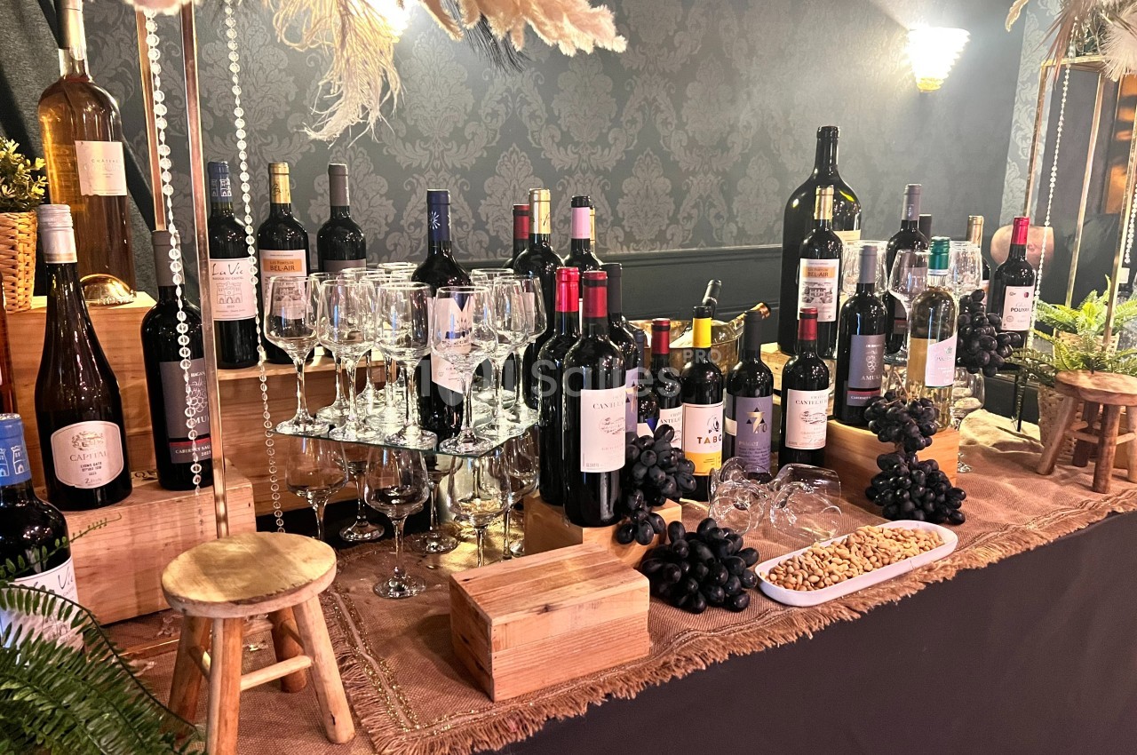 Table garnie de bouteilles de vin, verres, raisins noirs et amandes, décorée dans une ambiance élégante et chaleureuse.