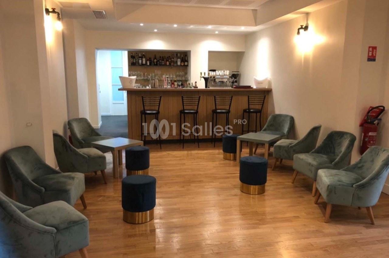 Salle avec un bar en bois, des fauteuils verts, des tabourets bleus et un sol en parquet clair.
