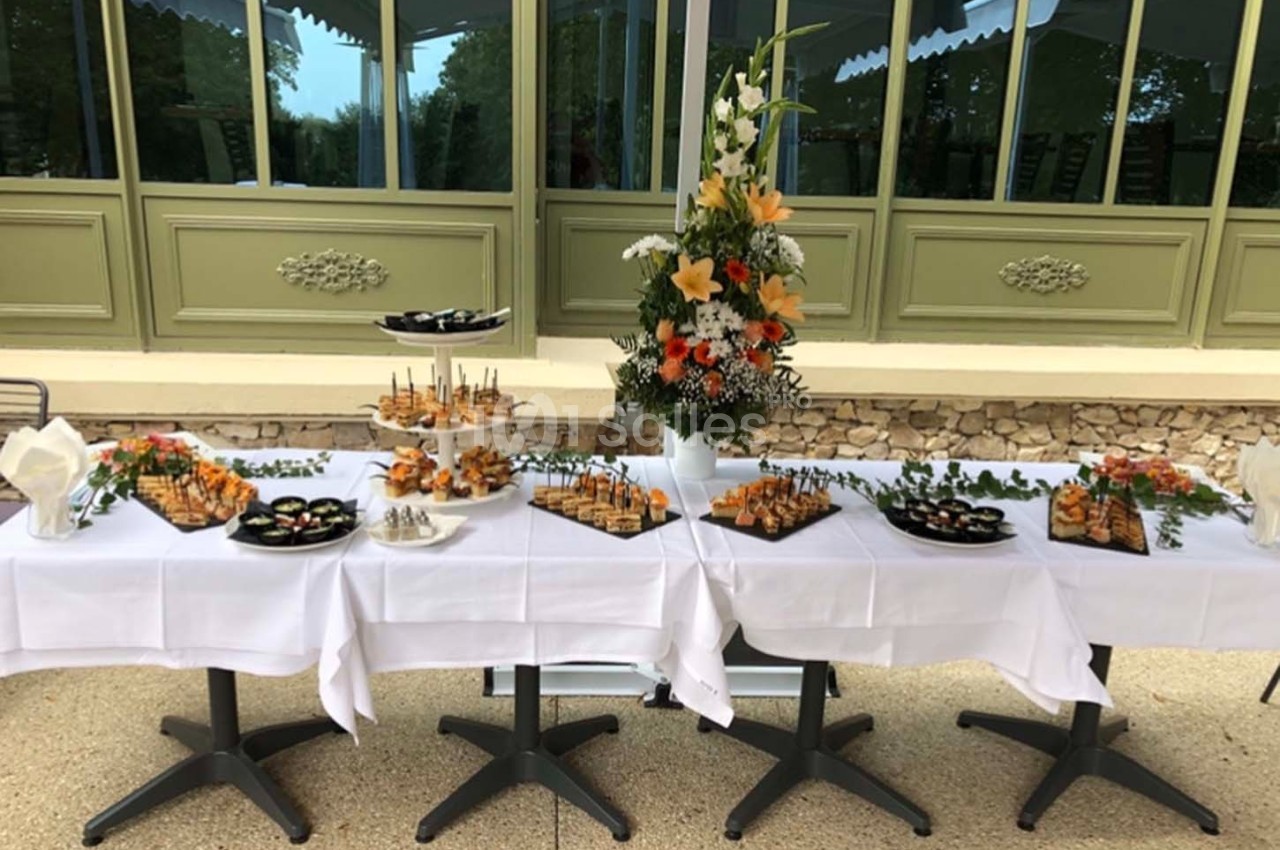 Table dressée avec des plateaux de bouchées apéritives variées, décorée de fleurs, devant une baie vitrée.