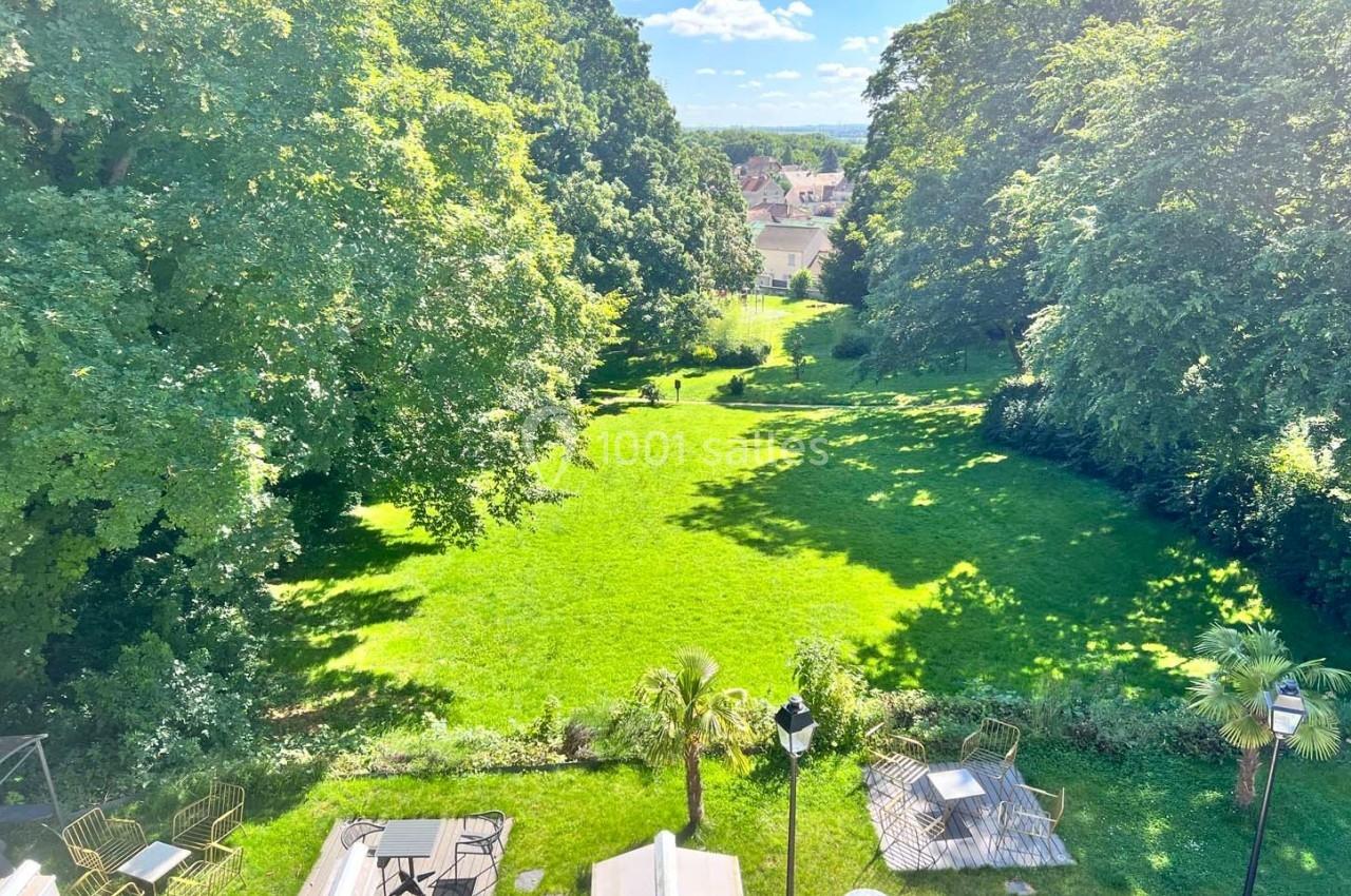 Vue d'un jardin verdoyant avec pelouse, arbres et mobilier de jardin sous un ciel bleu ensoleillé.