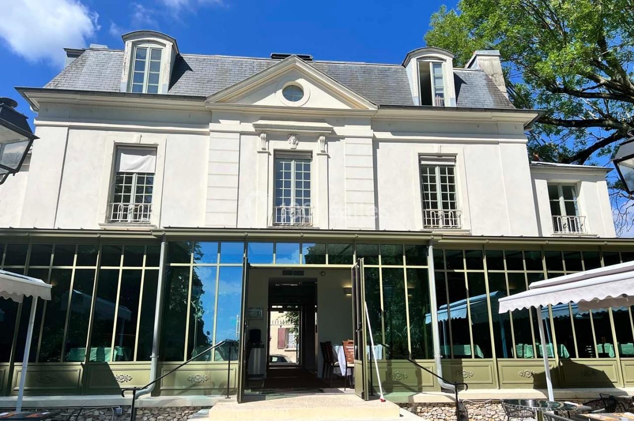 Façade d'un bâtiment ancien avec des grandes fenêtres et une terrasse extérieure sous un ciel bleu.