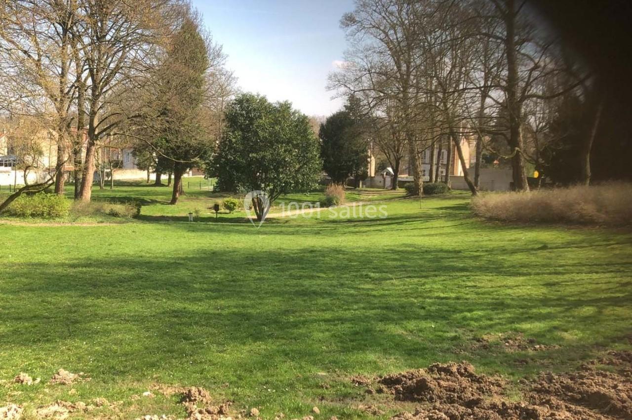 Pelouse verdoyante bordée d'arbres et de buissons, avec quelques bâtiments visibles en arrière-plan.