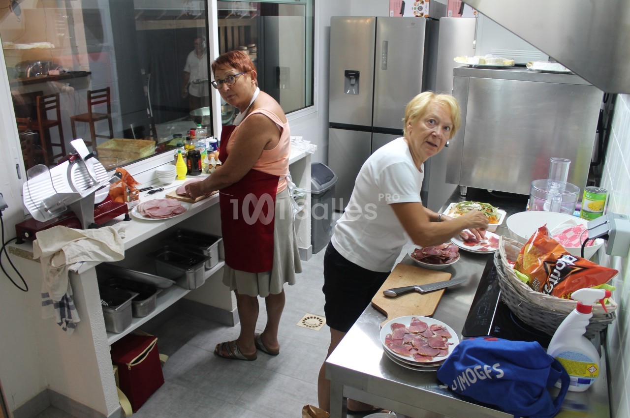 Deux femmes préparent des assiettes de charcuterie dans une cuisine professionnelle.