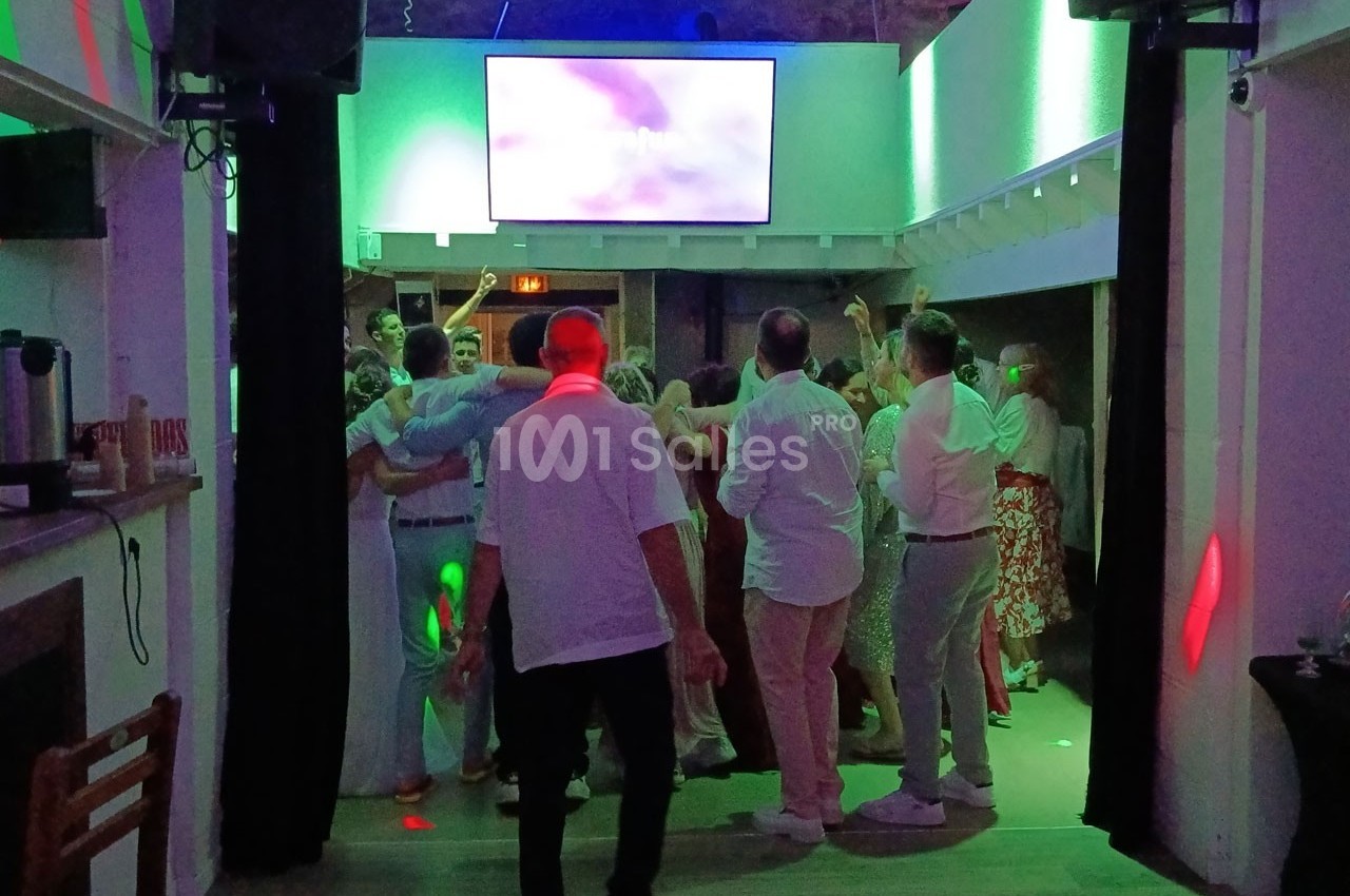 Groupe de personnes dansant dans une salle éclairée par des lumières colorées, avec un écran diffusant des images en arrière…