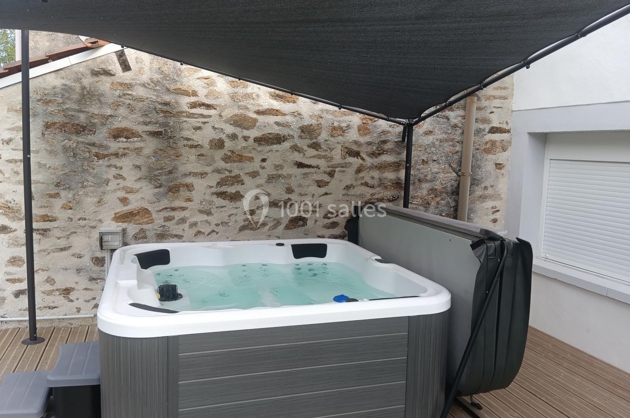 Spa extérieur rempli d'eau, installé sur une terrasse en bois, protégé par une toile d'ombrage noire.