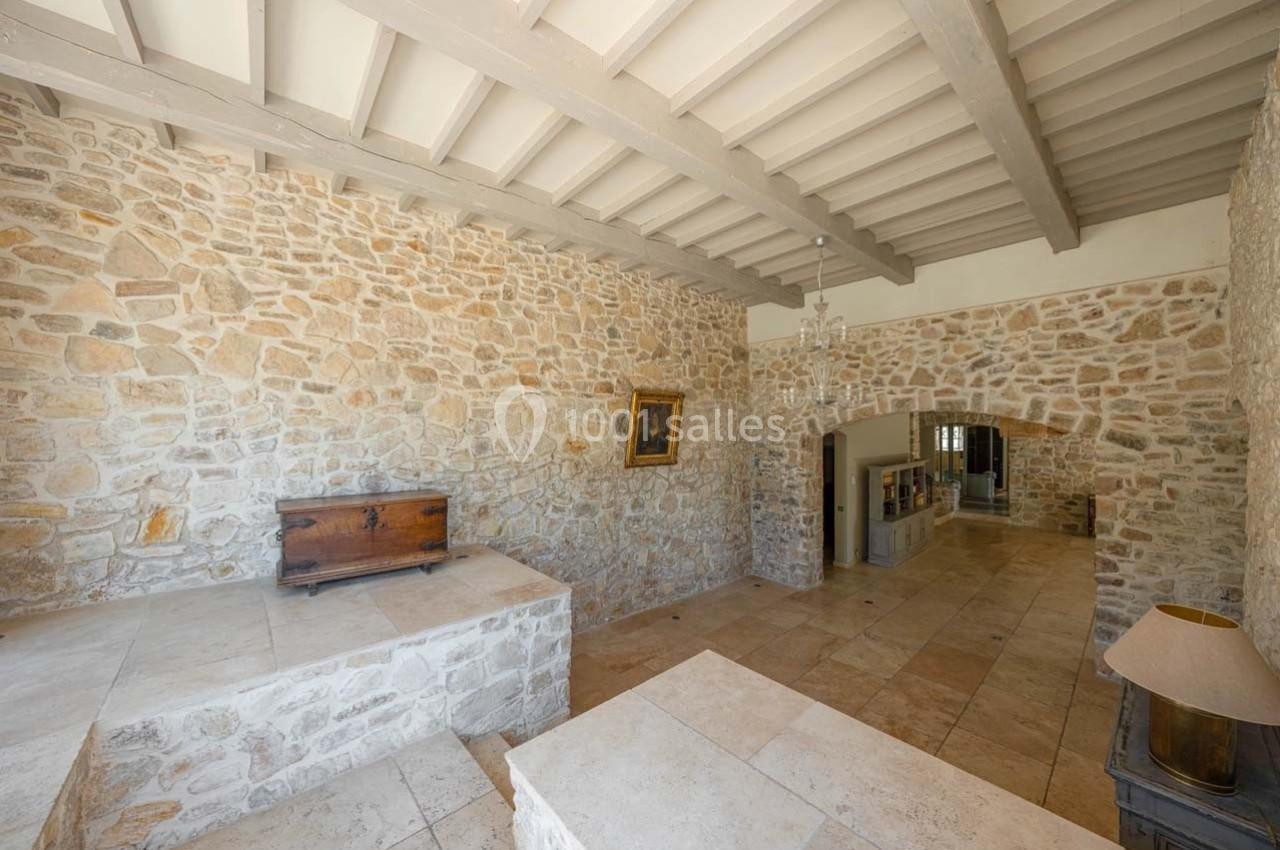 Mur en pierre apparente dans une pièce lumineuse avec plafond à poutres, sol en pierre et mobilier minimaliste.