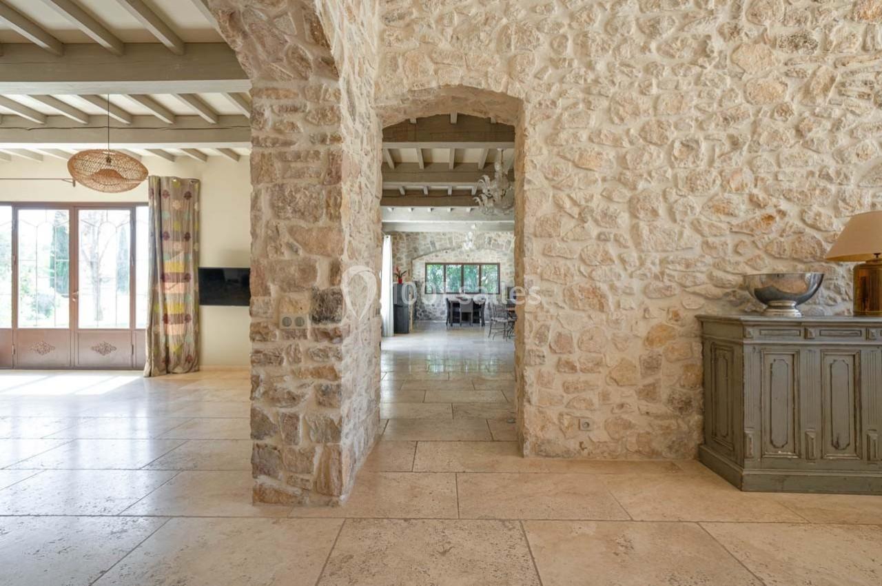 Intérieur lumineux avec murs en pierre apparente, sol en pierre claire, et vue sur une salle à manger au fond.