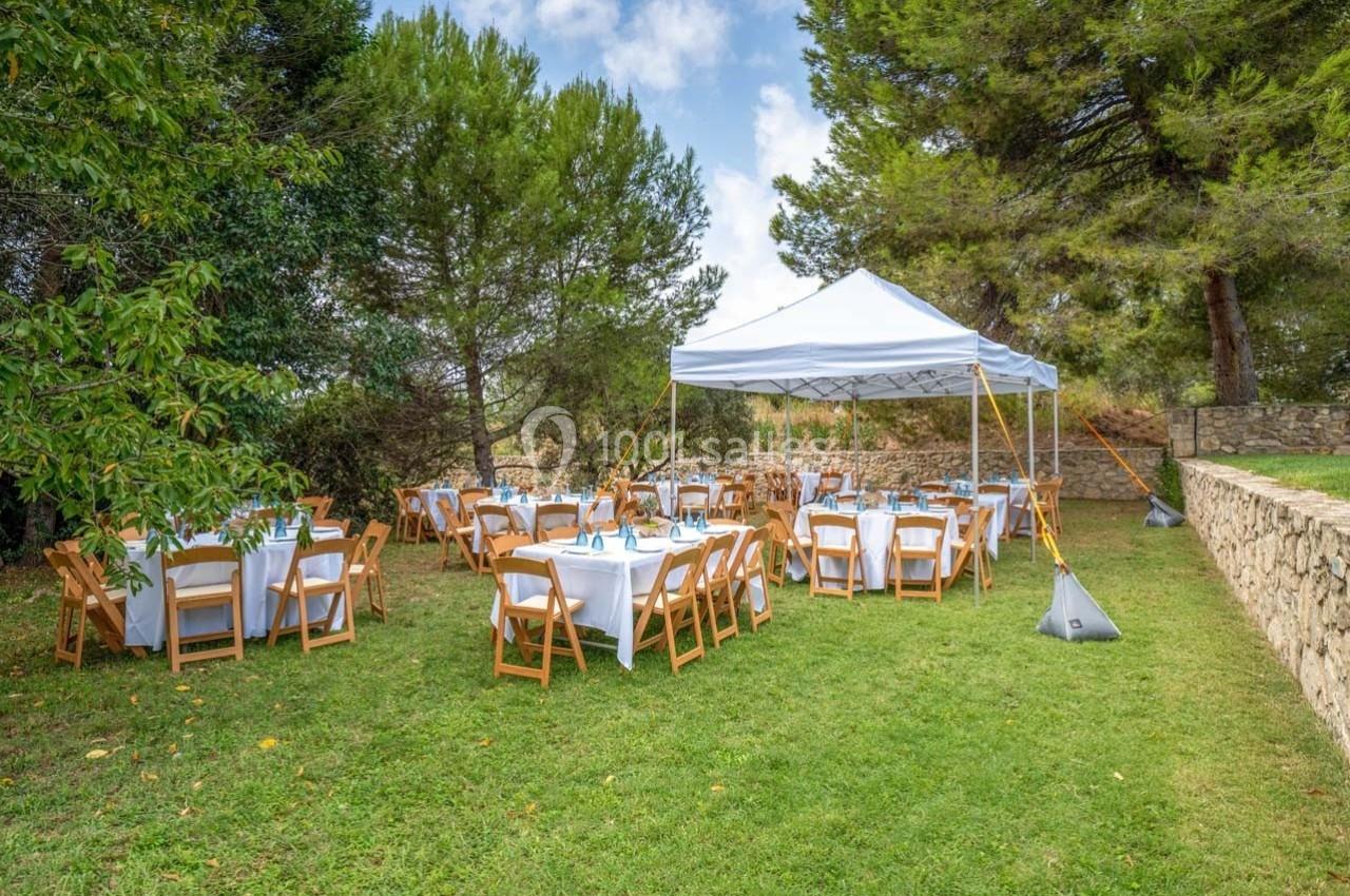 Tables dressées sous une tente blanche et à l'extérieur, entourées d'arbres et d'une pelouse verte.