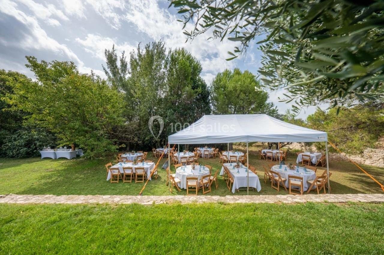 Tente blanche installée dans un jardin, abritant des tables dressées pour un événement en plein air.
