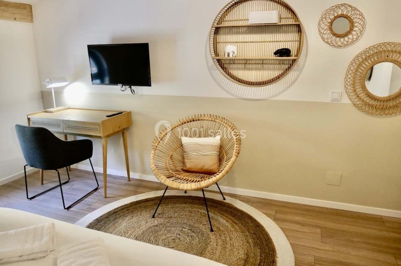 Coin bureau avec chaise noire, bureau en bois clair, fauteuil en rotin, étagères murales rondes et télévision fixée au mur.