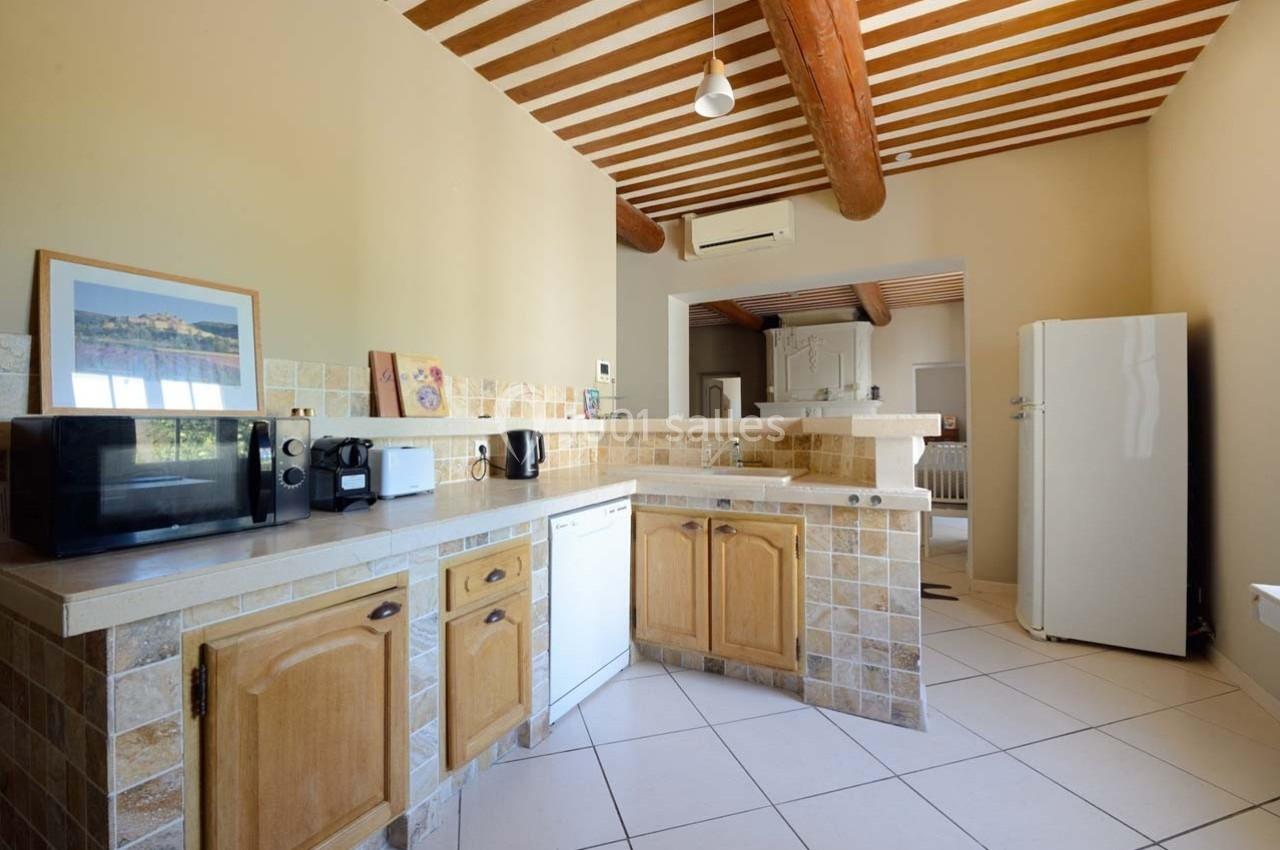 Cuisine lumineuse avec poutres apparentes, électroménagers modernes, carrelage beige et meubles en bois clair.