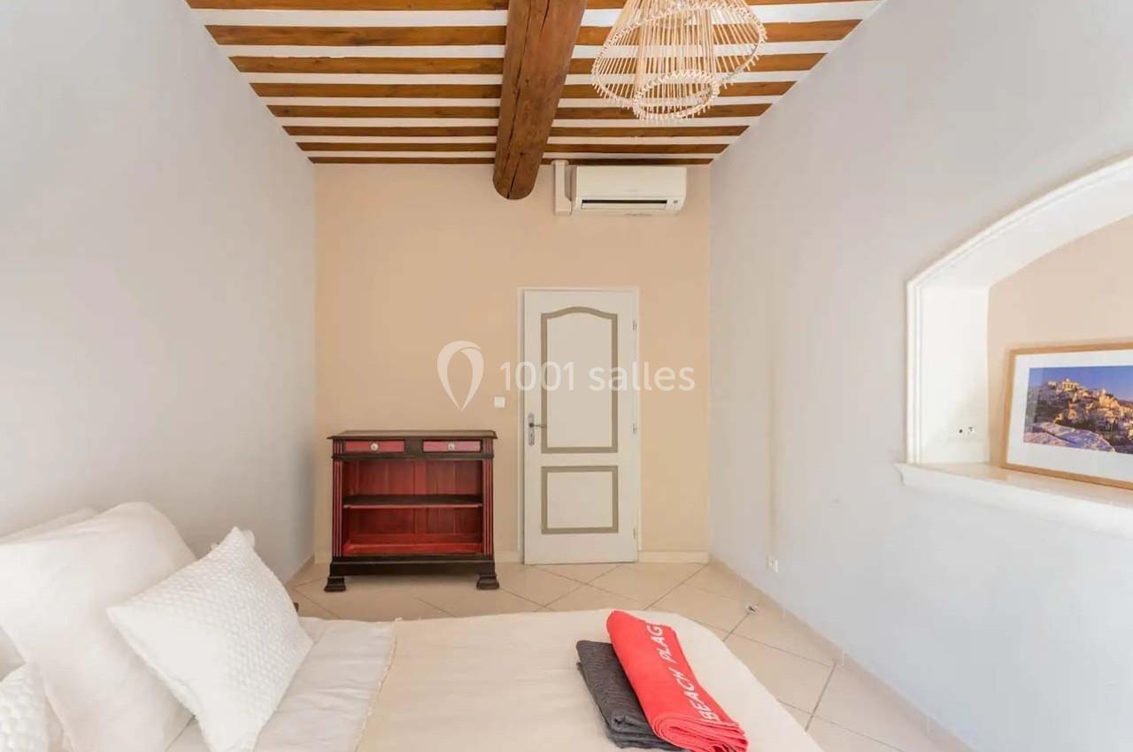 Chambre lumineuse avec lit double, poutres apparentes, meuble en bois, climatisation et décoration minimaliste.