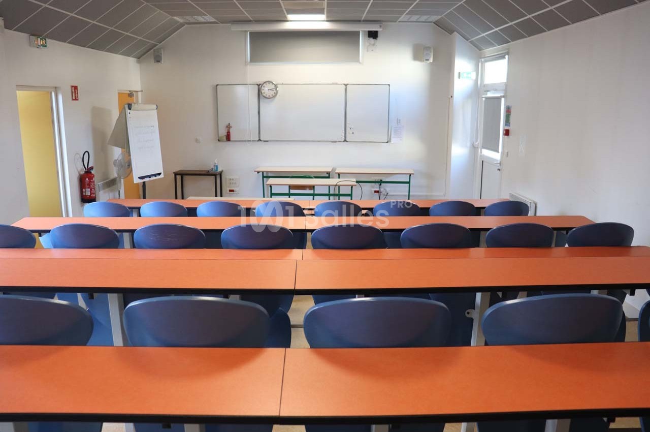 Salle de classe vide avec des rangées de tables et chaises, tableau blanc et horloge murale en arrière-plan.