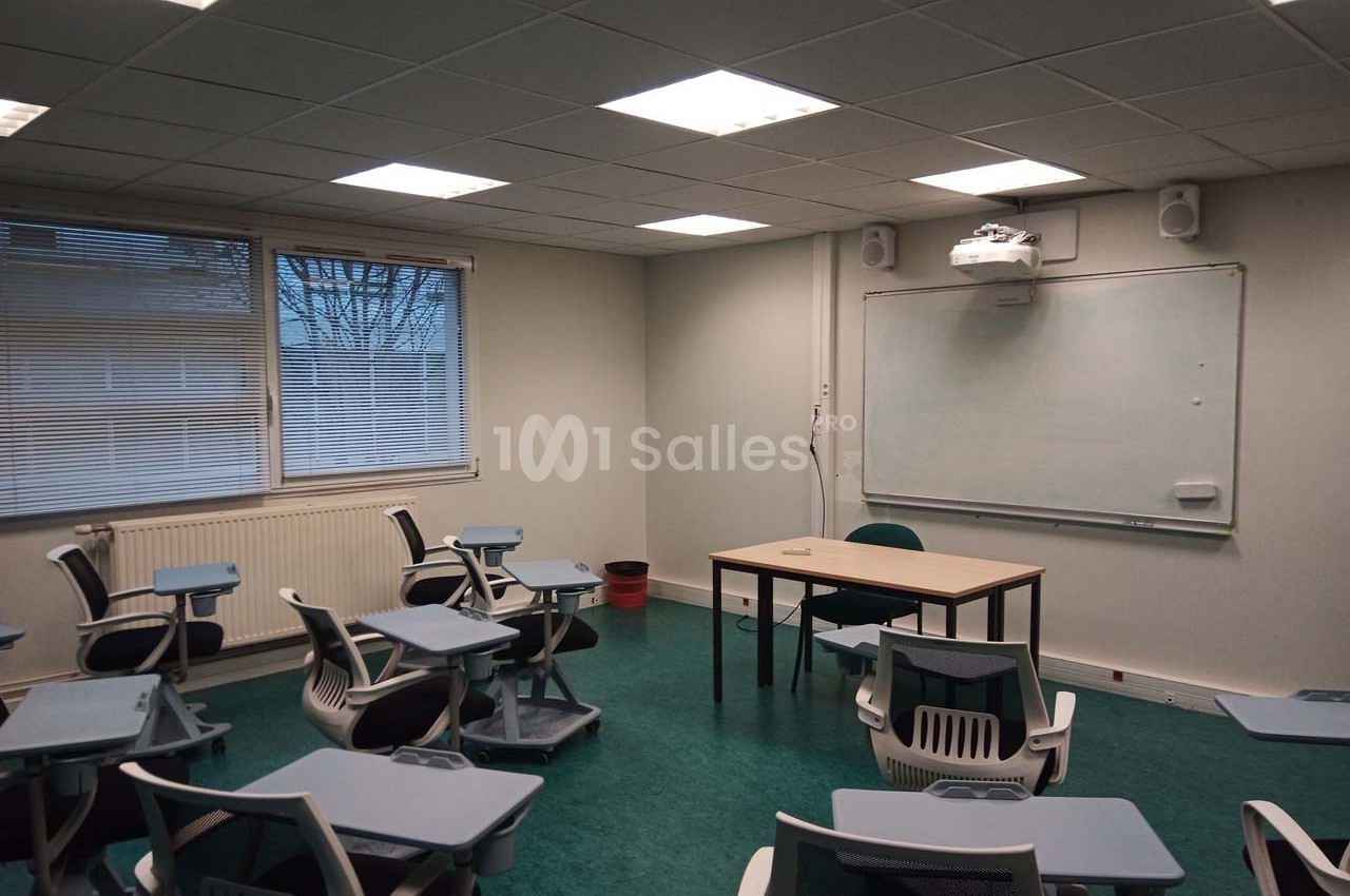 Salle de classe vide avec des chaises équipées de tablettes, un tableau blanc et un projecteur au plafond.