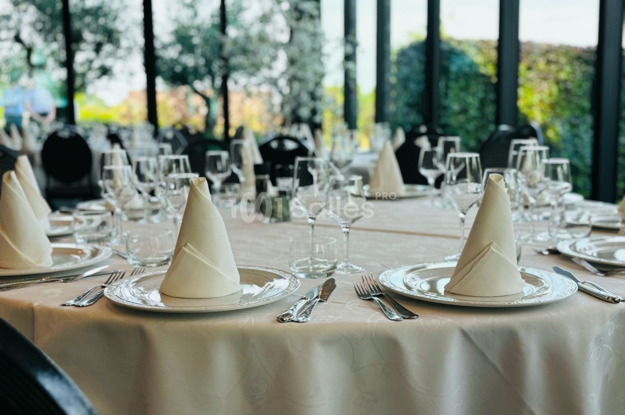 Table élégamment dressée avec nappes blanches, serviettes pliées, verres et couverts dans une salle lumineuse avec vue sur…