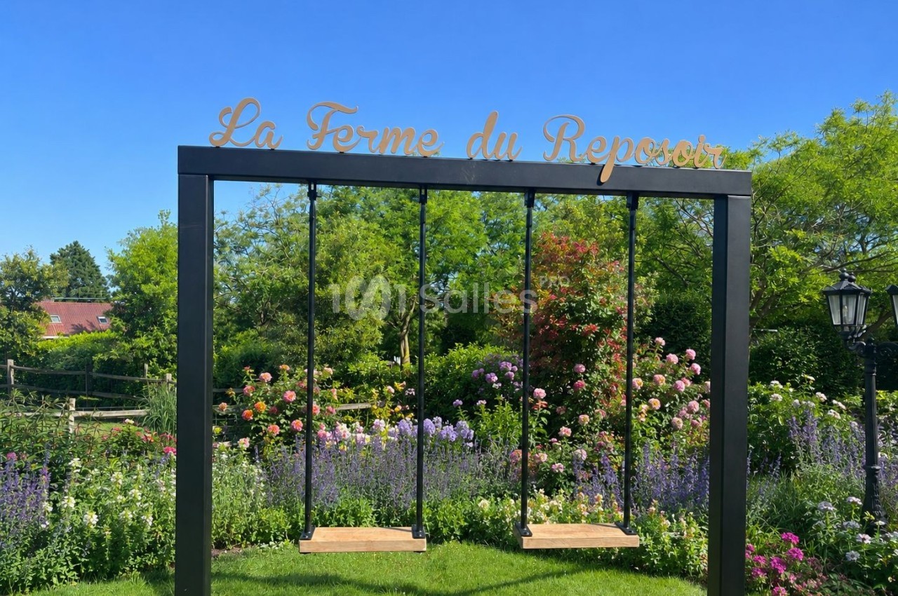 Deux balançoires en bois suspendues dans un cadre métallique, entourées de fleurs et de verdure sous un ciel bleu.