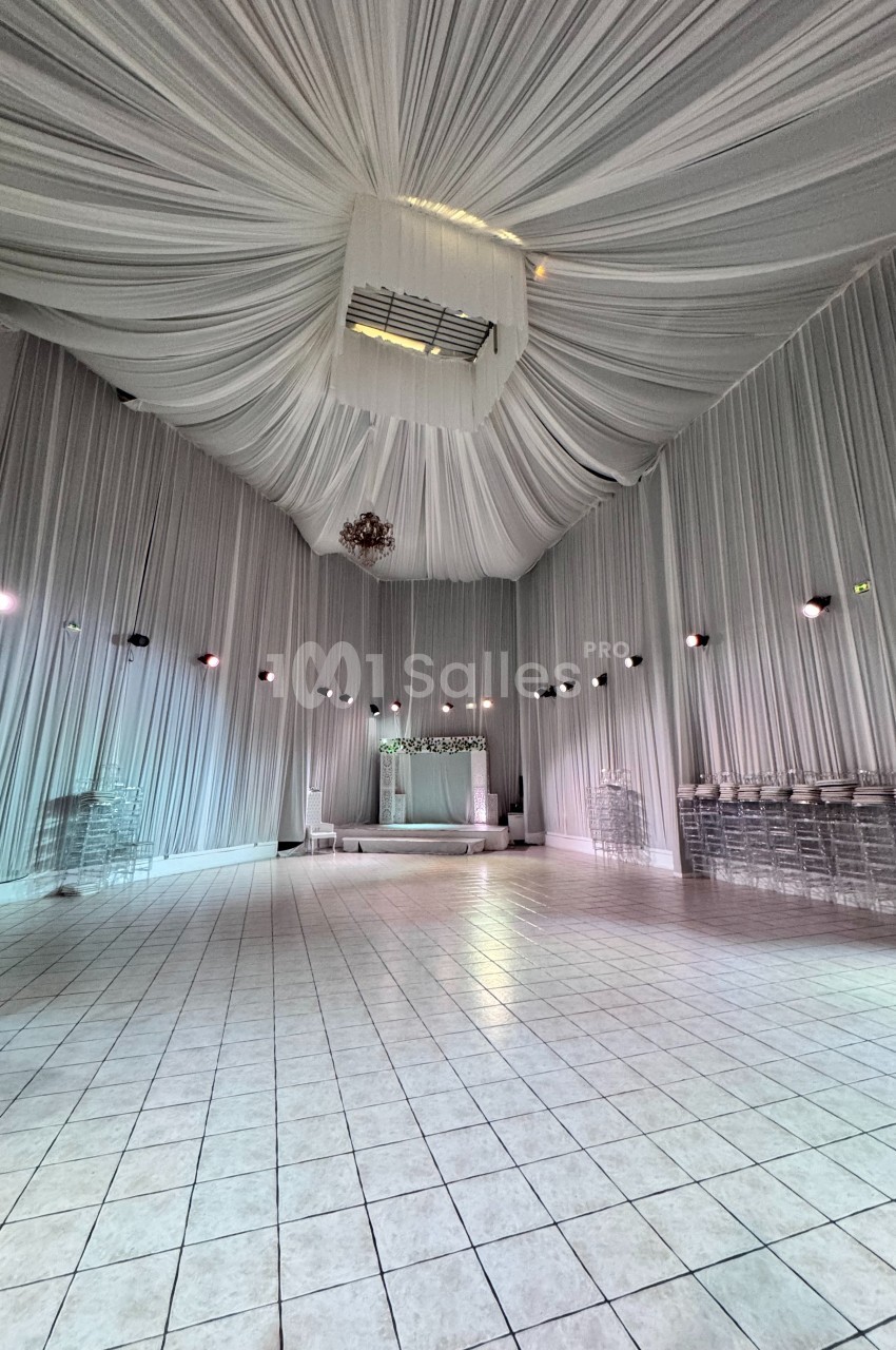Salle de réception spacieuse avec plafond drapé de tissu blanc, murs éclairés et sol carrelé.