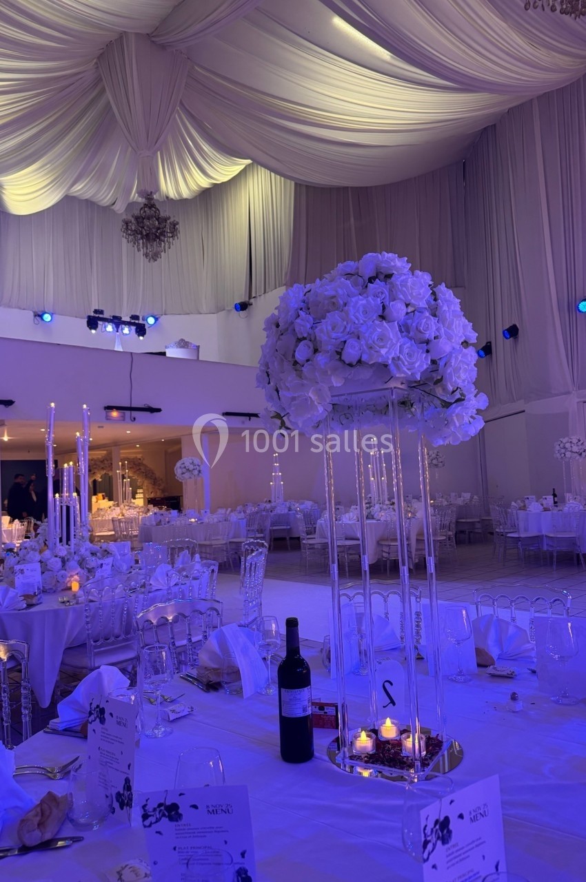 Salle de réception décorée avec des tables élégantes, centre de table floral, chandeliers et éclairage tamisé.