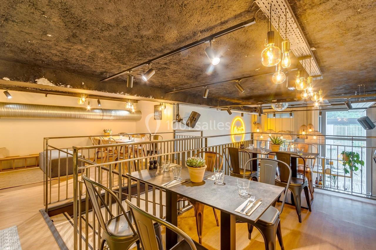 Salle de restaurant moderne avec tables dressées, chaises en métal, éclairage suspendu et décor industriel.