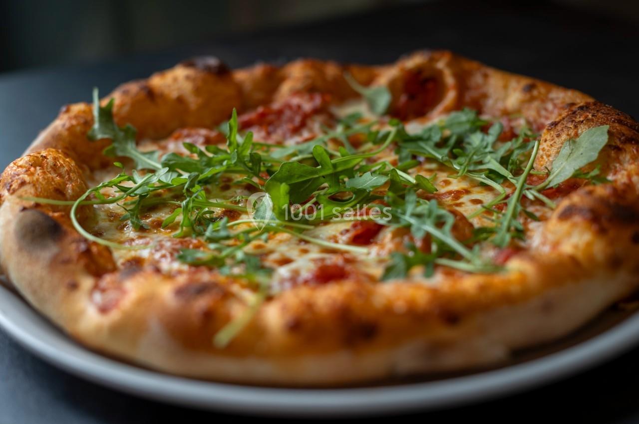 Pizza garnie de roquette fraîche, fromage fondu et sauce tomate, servie sur une assiette blanche.