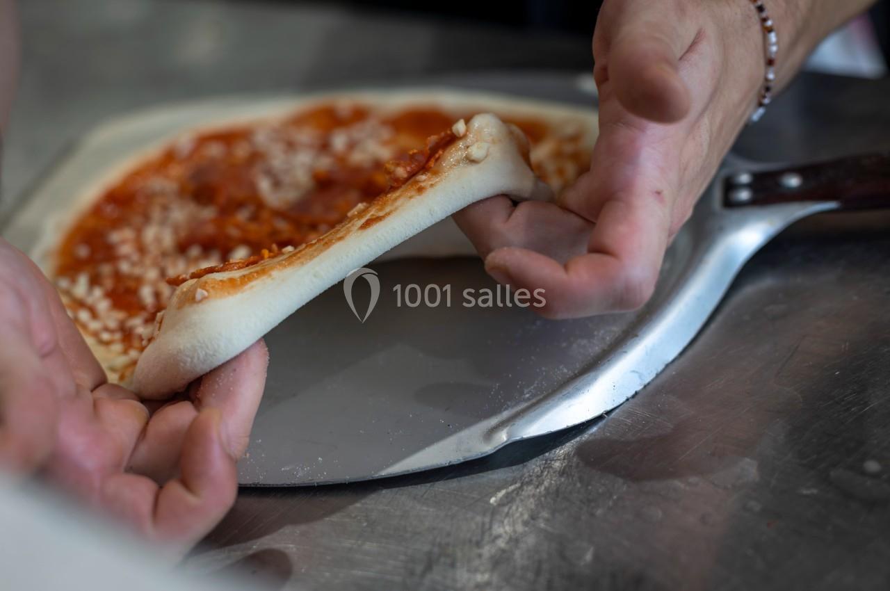 Un pizzaiolo étire une pâte à pizza garnie de sauce tomate sur une pelle en métal.