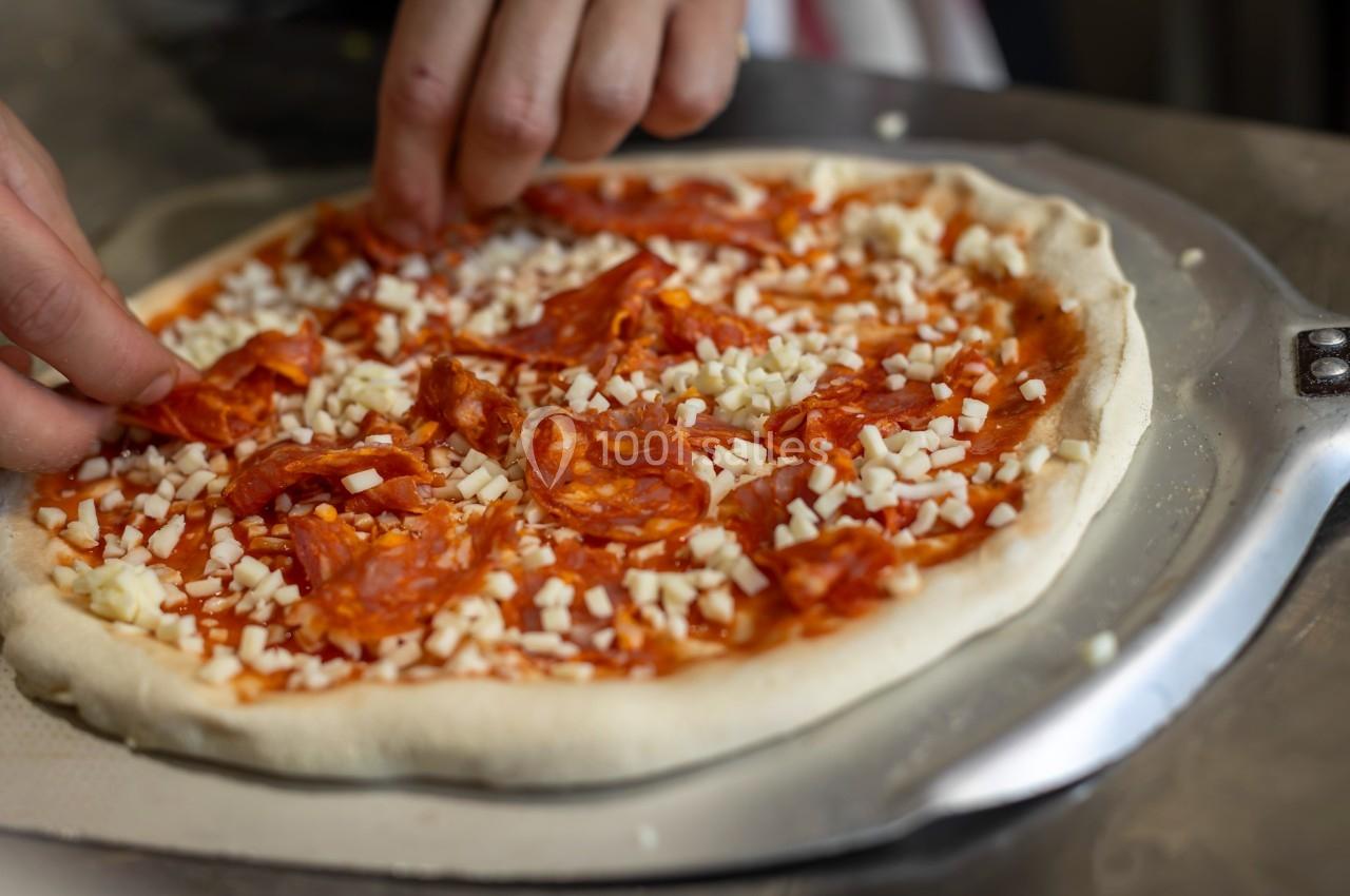 Préparation d'une pizza avec des mains ajoutant des tranches de chorizo sur une pâte garnie de sauce tomate et fromage râpé.