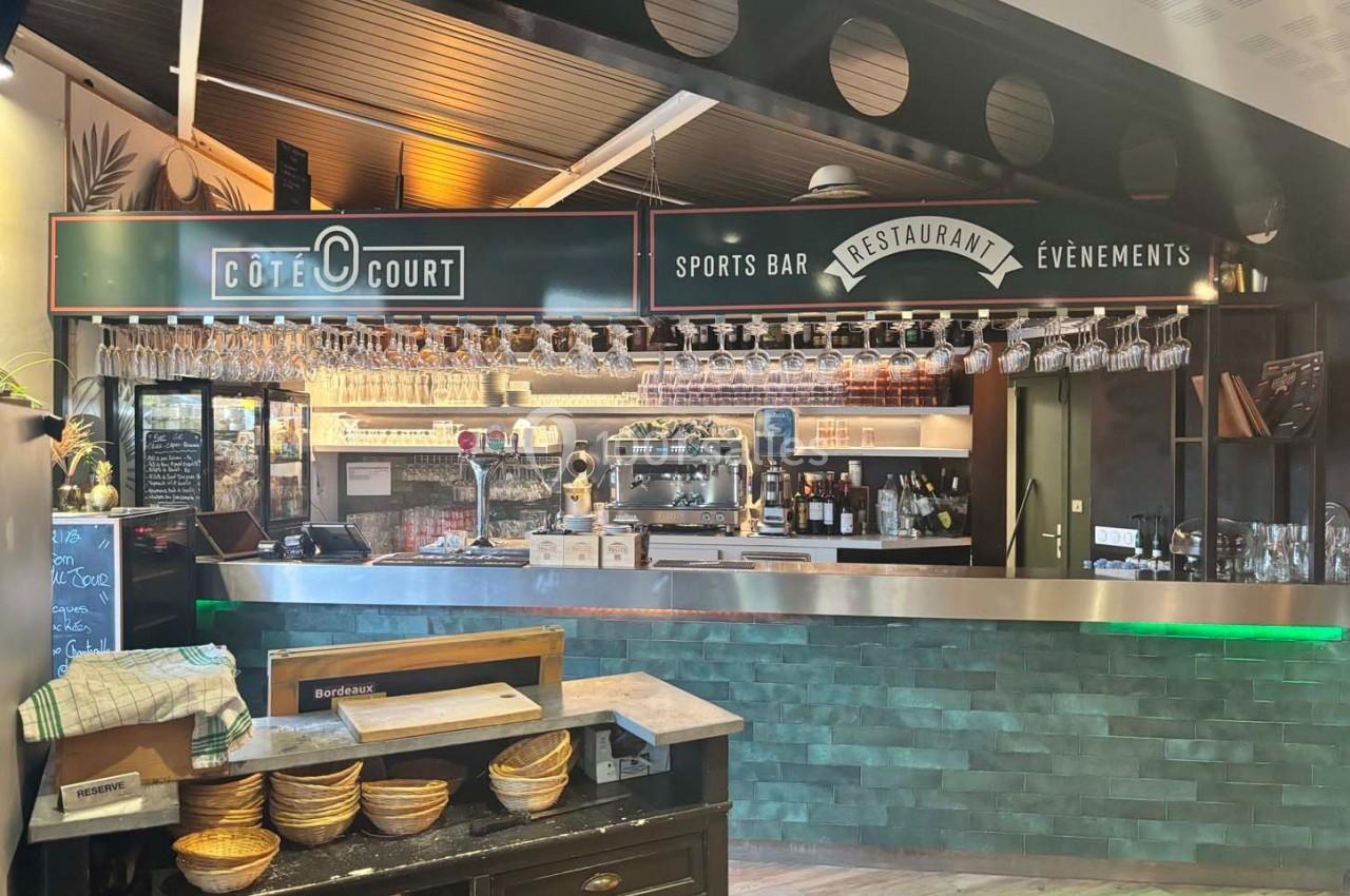 Comptoir d'un bar-restaurant avec étagères de verres suspendus, enseigne ’Côté Court’ et ambiance moderne.
