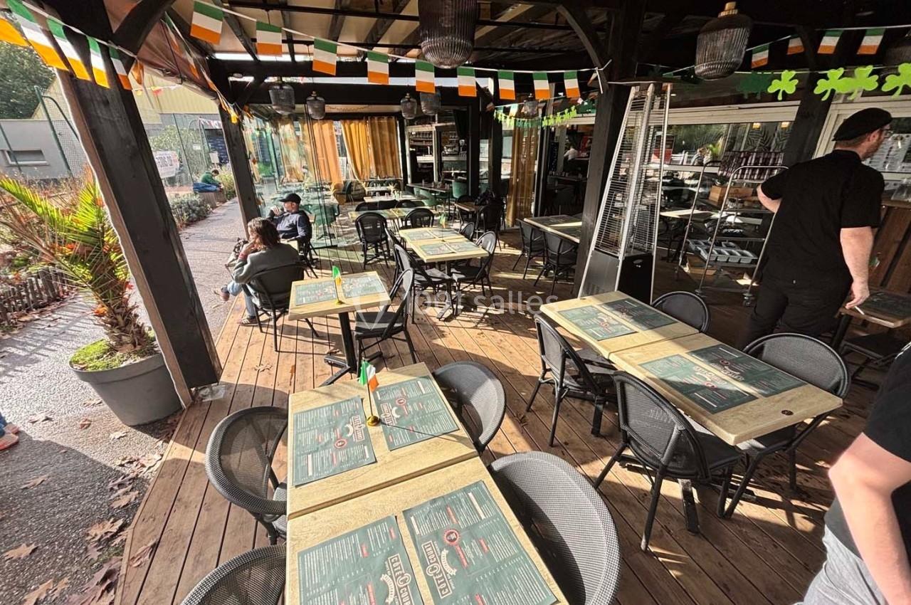 Terrasse en bois d'un restaurant décorée de fanions irlandais, avec tables dressées et quelques clients assis.