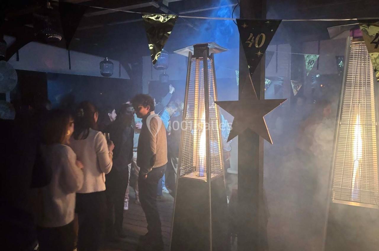 Personnes rassemblées dans une ambiance festive avec des chauffages extérieurs allumés et des décorations suspendues.