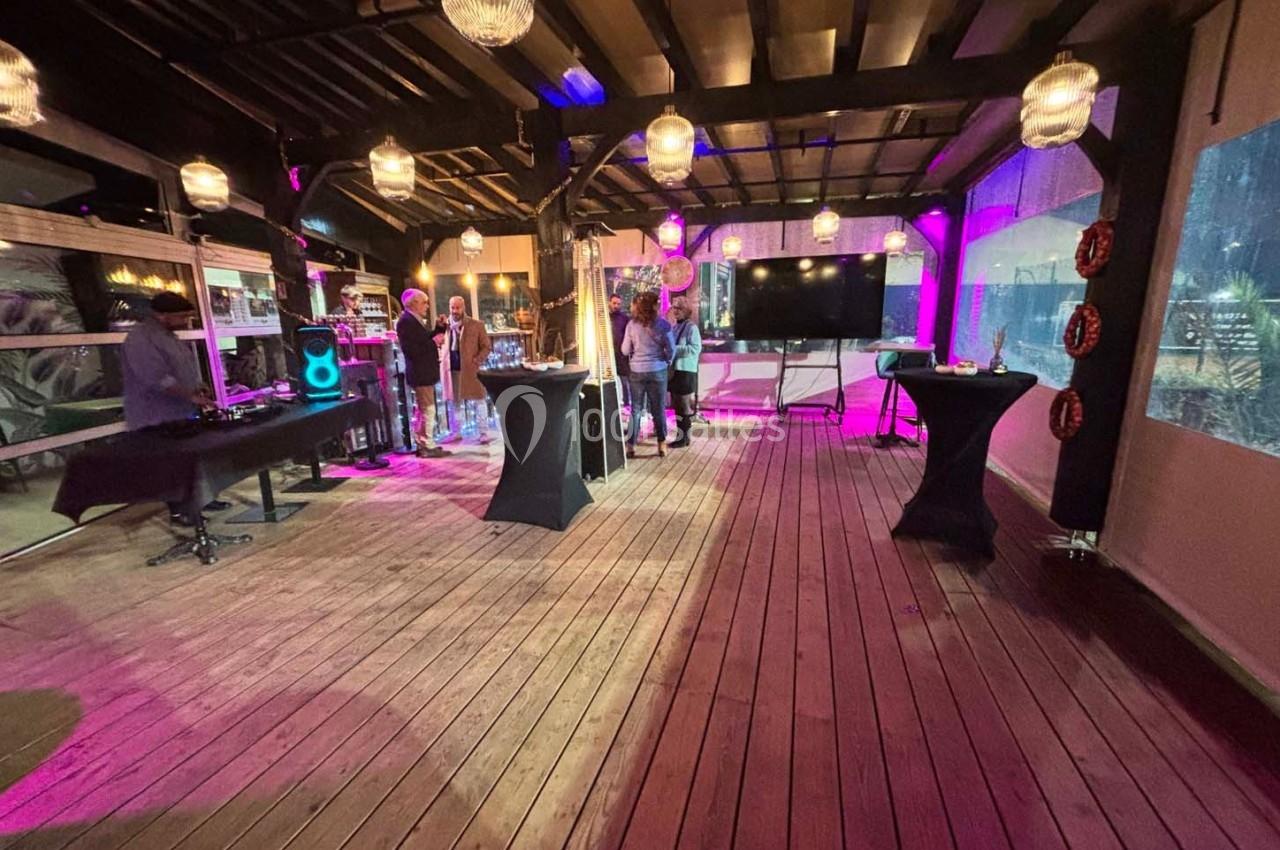 Espace intérieur en bois avec éclairage tamisé, tables hautes, écran et matériel de sonorisation, ambiance événementielle.