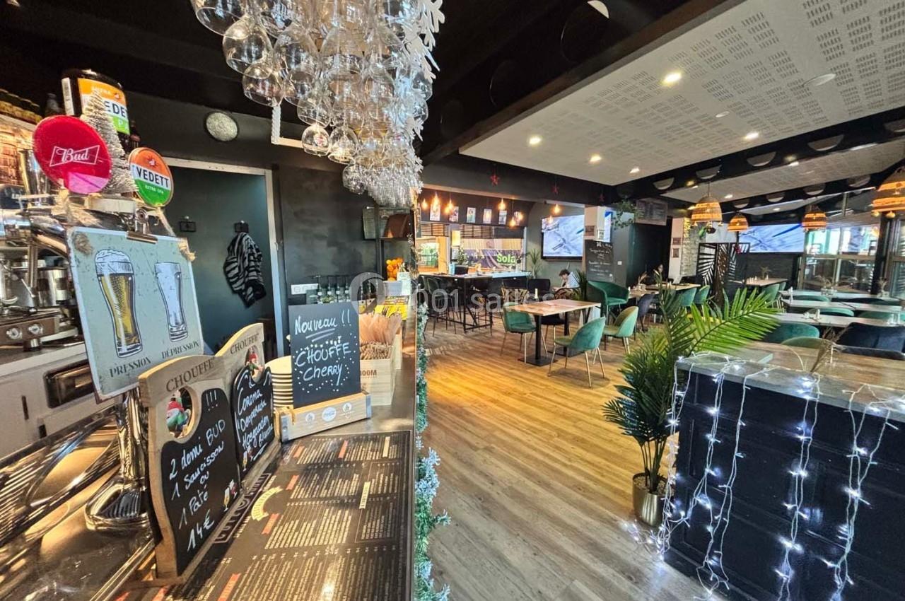 Intérieur d'un bar-restaurant avec comptoir, tables, chaises et décorations lumineuses dans une ambiance chaleureuse.