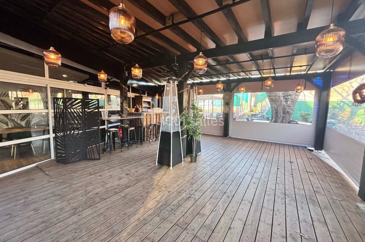 Terrasse en bois couverte avec des lampes suspendues, un bar, des tables hautes et des plantes décoratives.