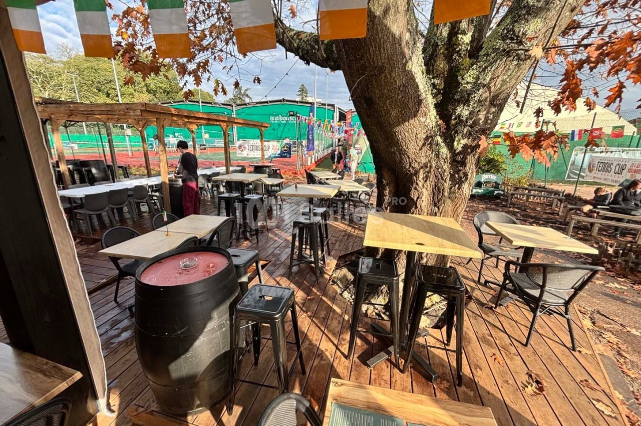 Terrasse en bois avec tables et chaises, décorée de fanions colorés, près d'un arbre en automne.
