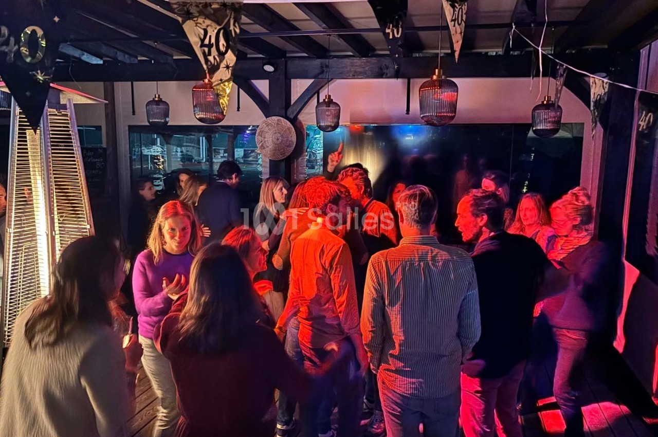 Groupe de personnes dans une ambiance festive avec éclairage coloré, décorations suspendues et chauffage extérieur.