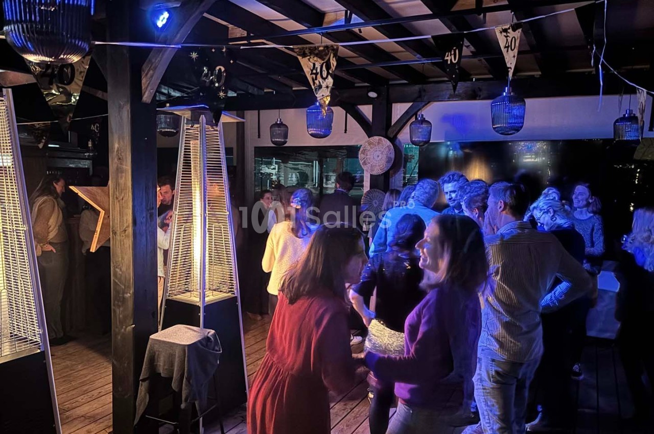 Groupe de personnes discutant et dansant dans un espace couvert décoré, éclairé par des lumières tamisées.