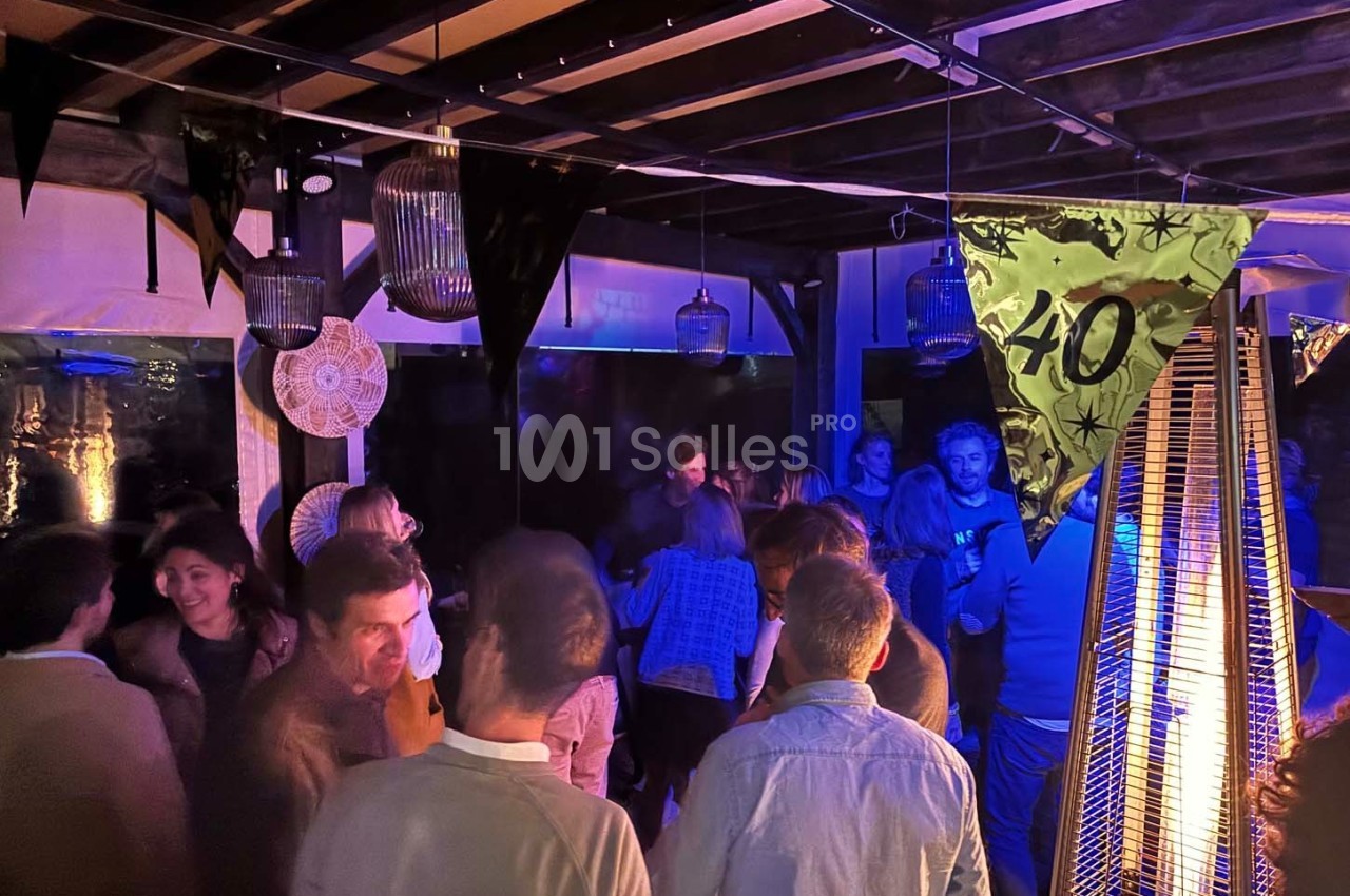 Groupe de personnes discutant et dansant lors d'une fête en soirée, sous une lumière tamisée et des décorations.