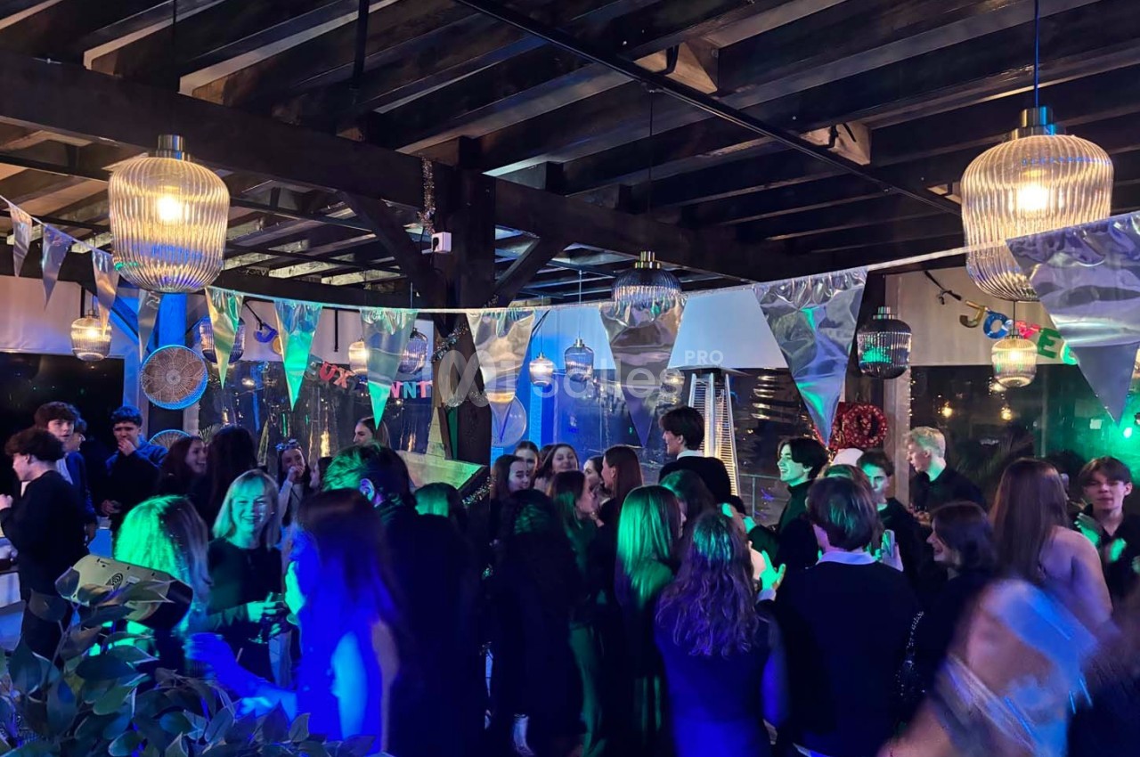 Groupe de personnes dans une salle décorée, éclairée par des lumières colorées, lors d'un événement festif en soirée.