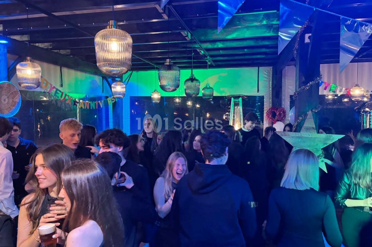 Des personnes dansent et discutent lors d'une soirée festive éclairée par des lumières colorées et des décorations…