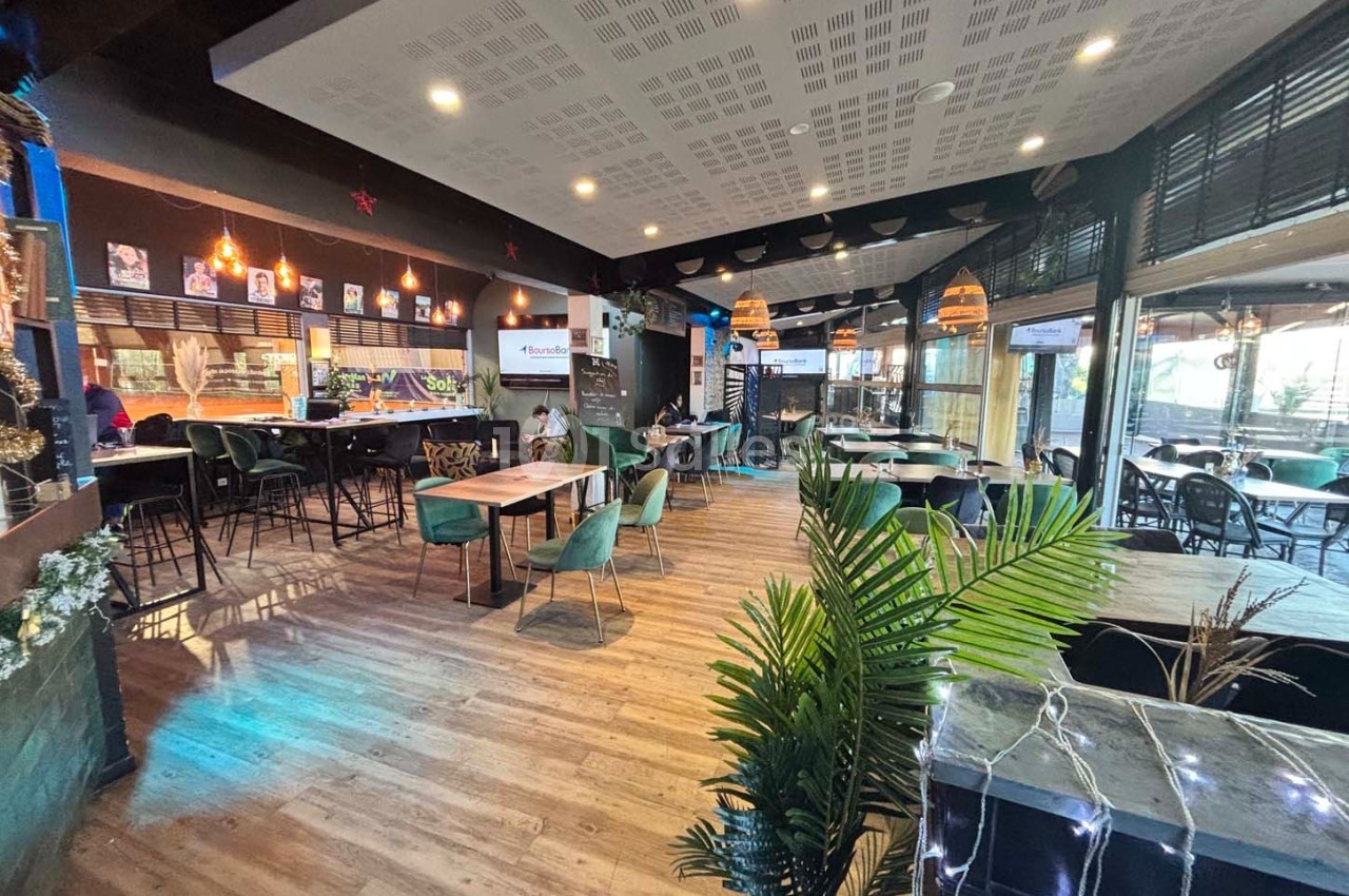 Intérieur d'un restaurant moderne avec tables, chaises, plantes décoratives et éclairage chaleureux.