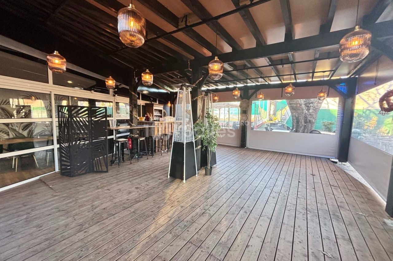 Terrasse couverte en bois avec des tables hautes, des lampes suspendues et des chauffages d'extérieur.