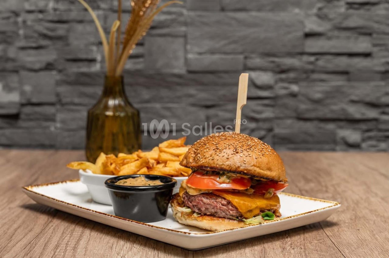 Burger garni de fromage, tomate et salade, accompagné de frites et d'une sauce, servi sur une assiette blanche.